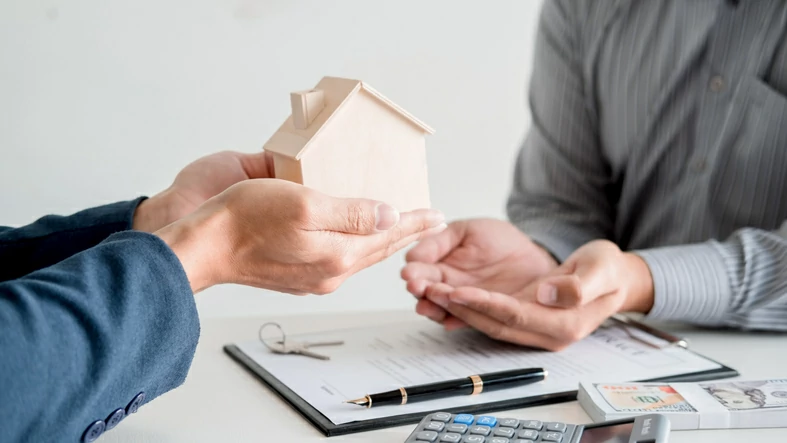 main tendant une maison en bois à une autre main en facee