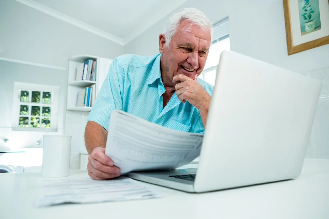 Homme âgé tenant un document et regardant dans un ordinateur portable