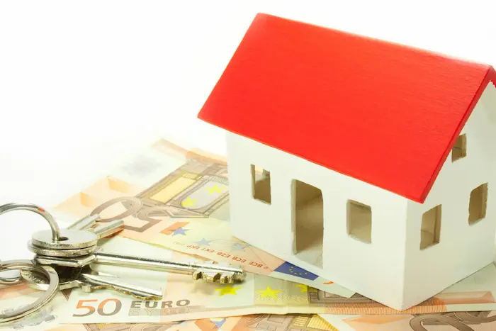 Clé de maison, billets en euros et une maquette de maison.