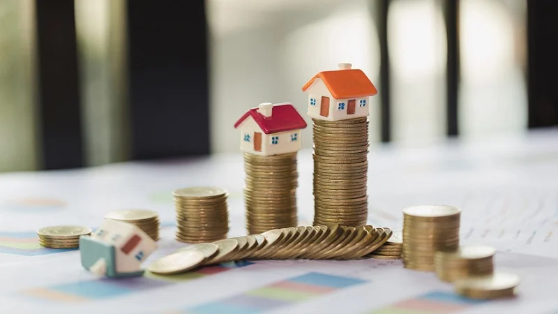 Maisons miniatures posées sur plusieurs piles de pièces de monnaie.
