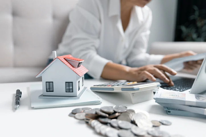 Femme utilisant un ordinateur portable à ôté d'une maquette de maison, de l'argent et une calculatrice.