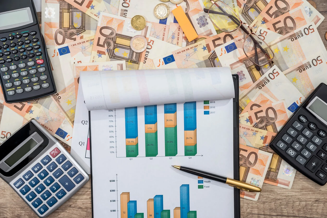 Bloc-notes, trois calculatrice et des billets de 50 euros éparpillés.