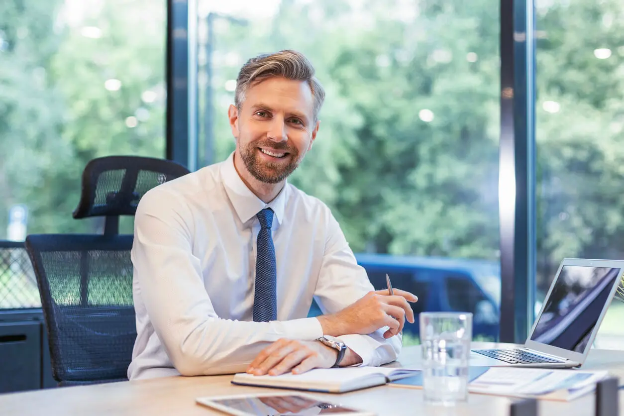 Un professionnel sur un bureau avec un agenda, un verre, un ordinateur portable et des documents.