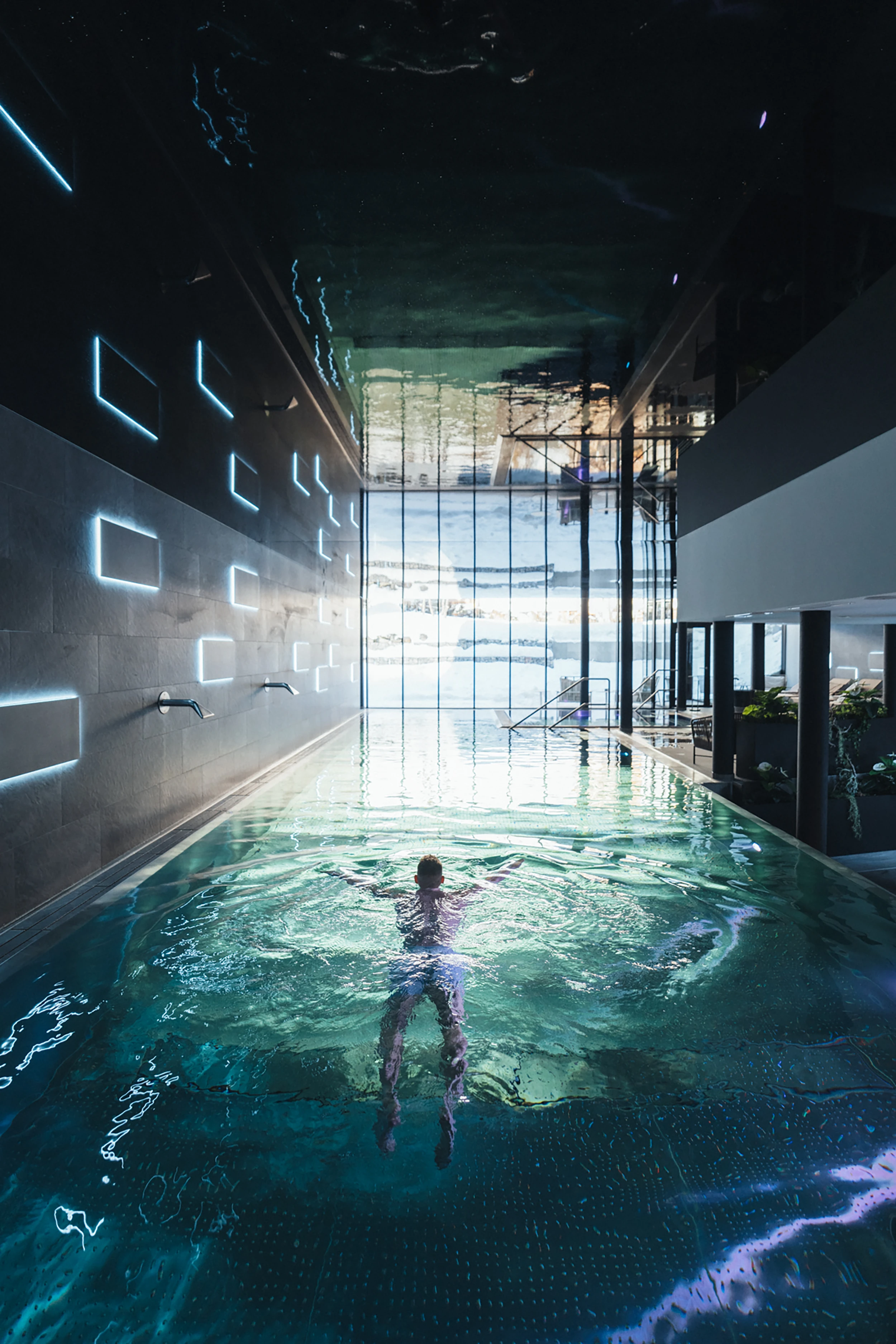 Gast schwimmt im beleuchteten Indoor-Pool mit Panoramafenster