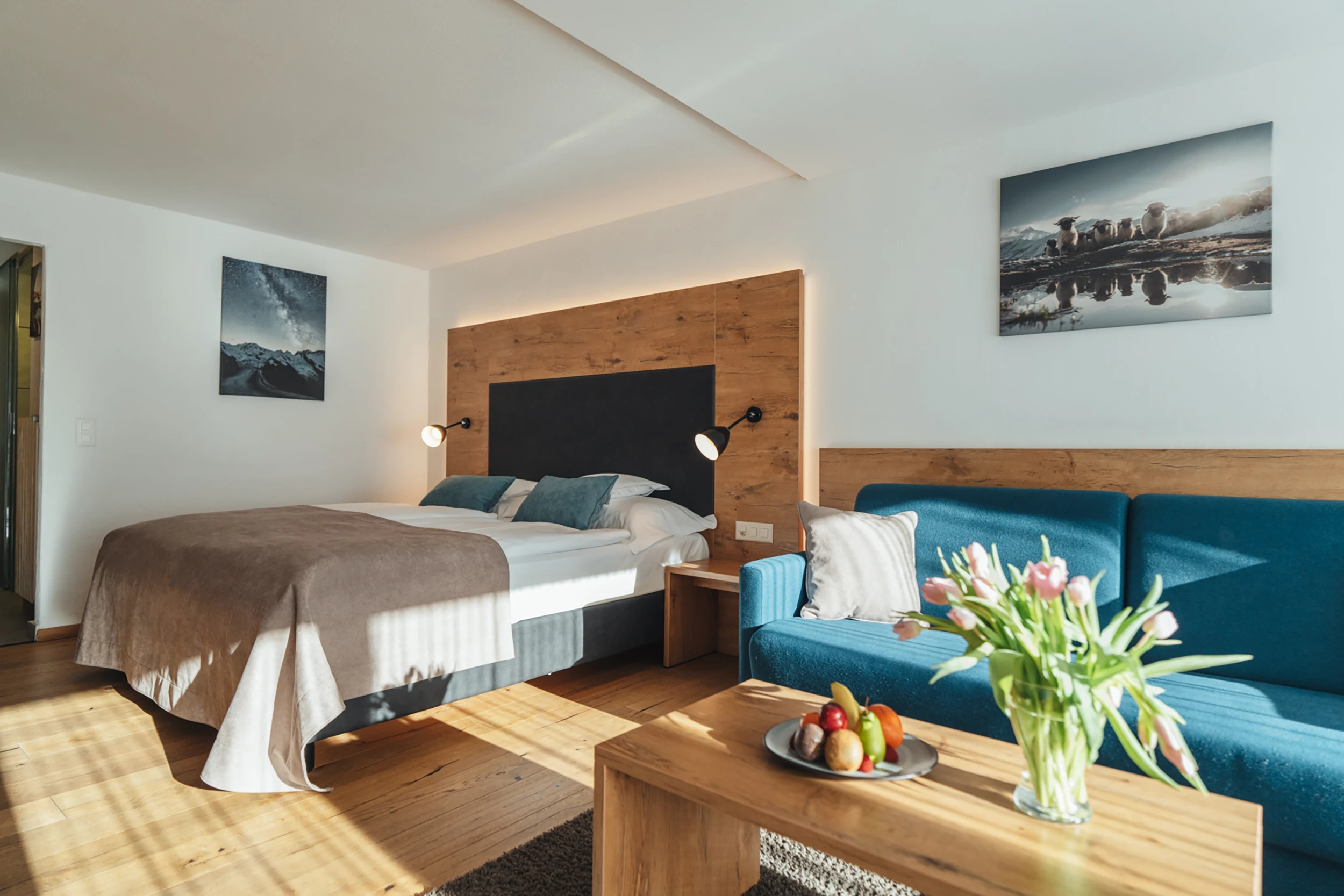 Helles Doppelzimmer mit blauem Sofa, Holzmöbeln und Tulpenstrauss