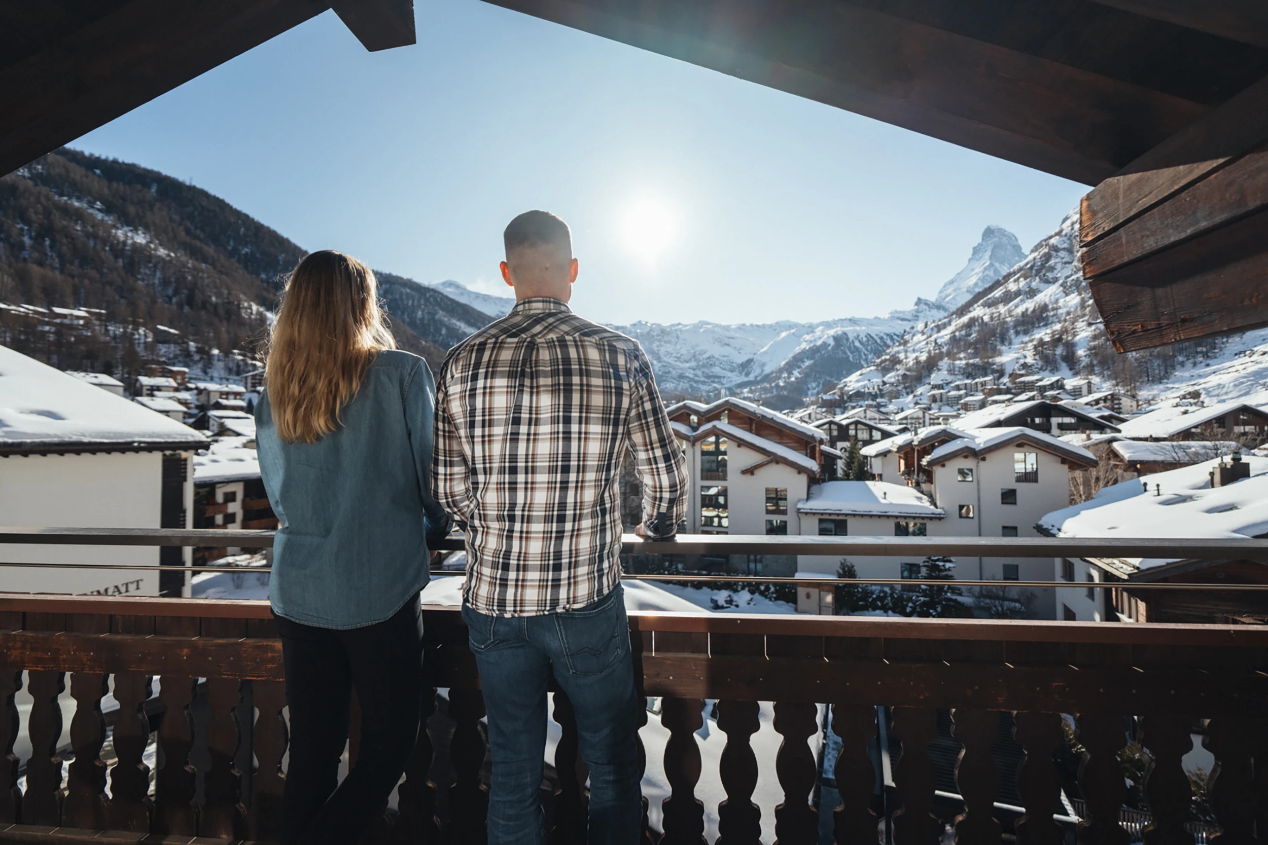 Paar auf dem Balkon blickt über die verschneiten Dächer von Zermatt zum Matterhorn