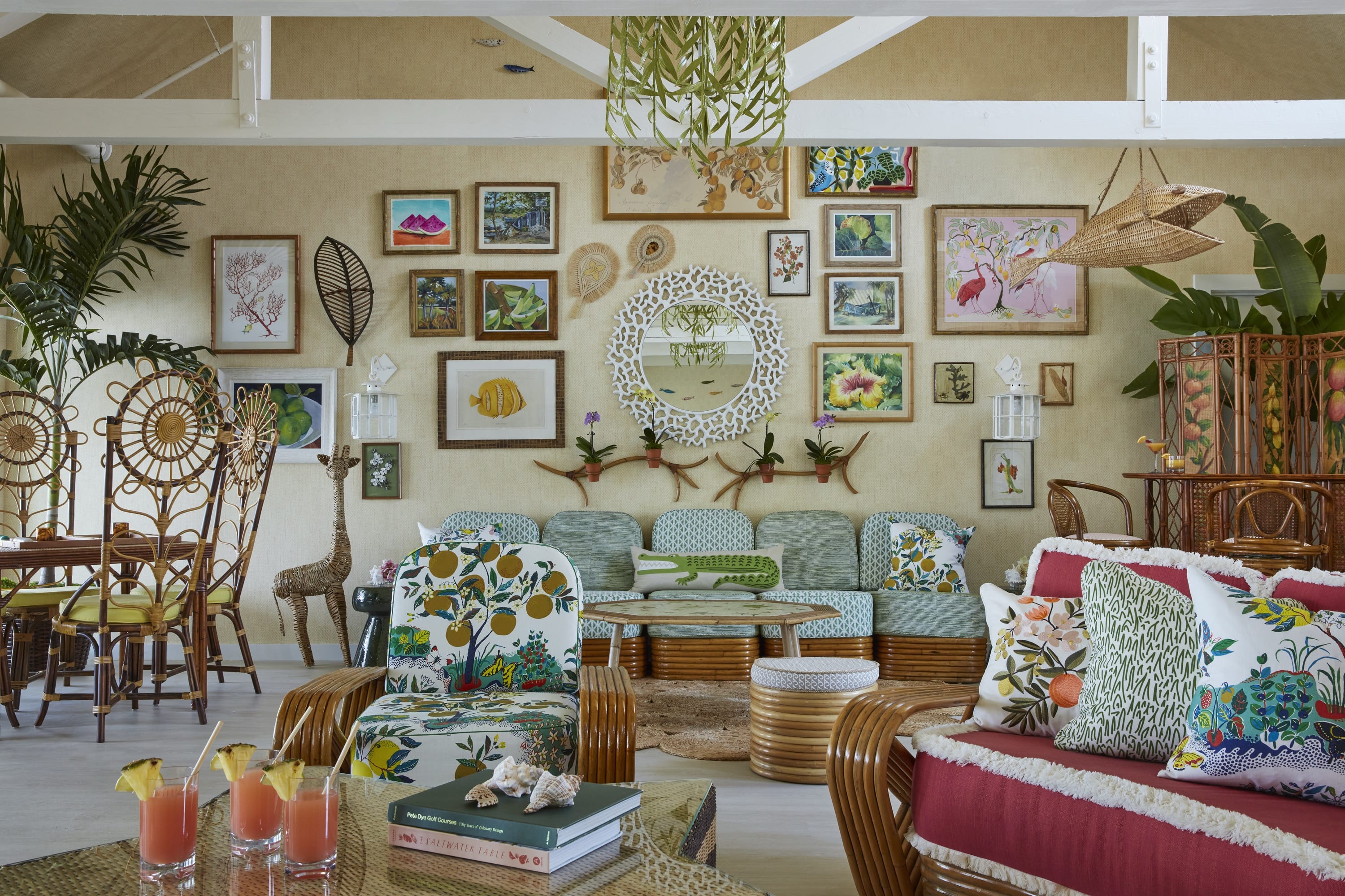 Tropical-themed living room with wicker furniture, colorful cushions, a gallery wall, and tropical drinks on a glass table.