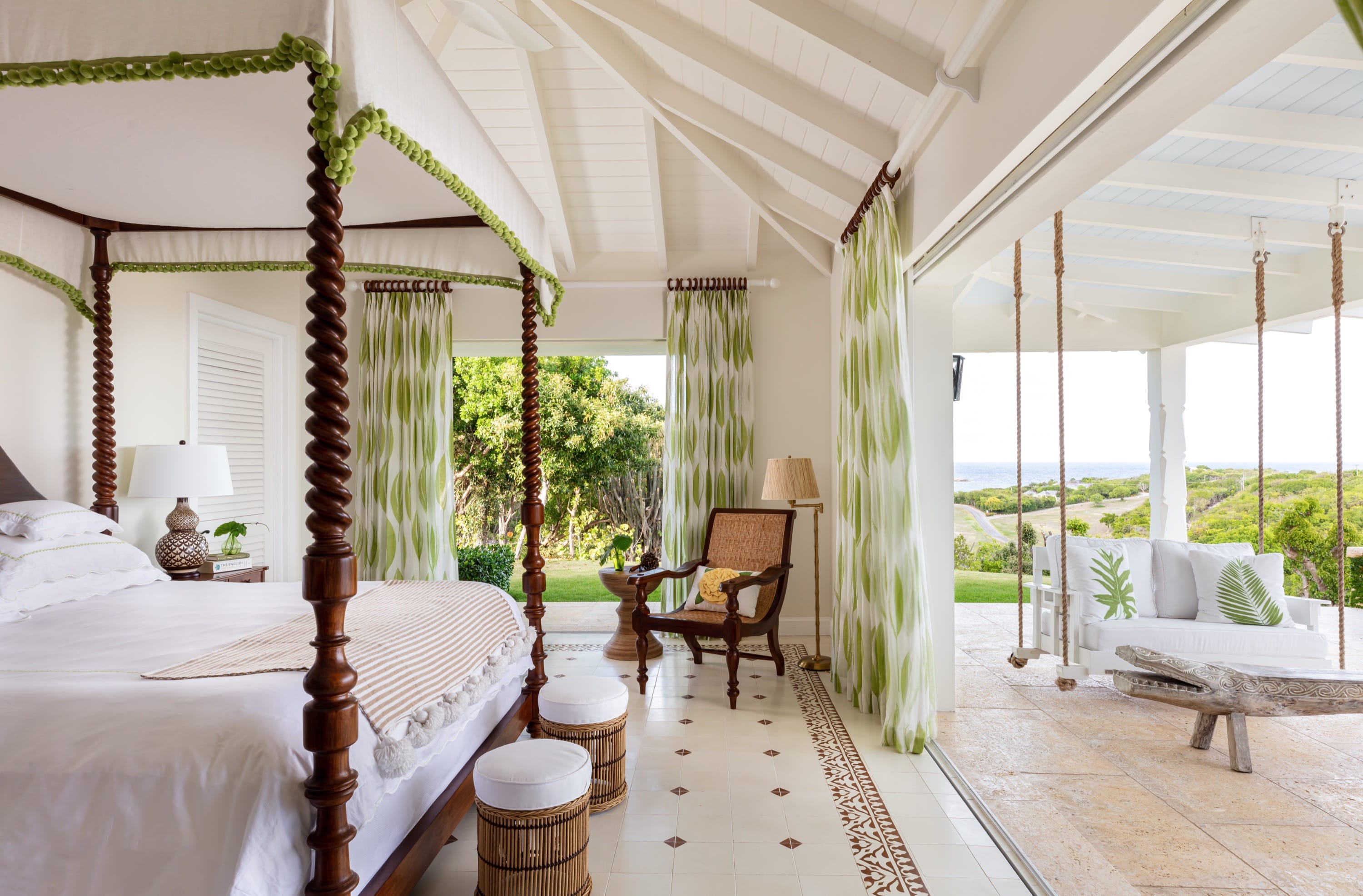 Bright bedroom with wooden four-poster bed, green patterned curtains, and outdoor swing sofa overlooking greenery.