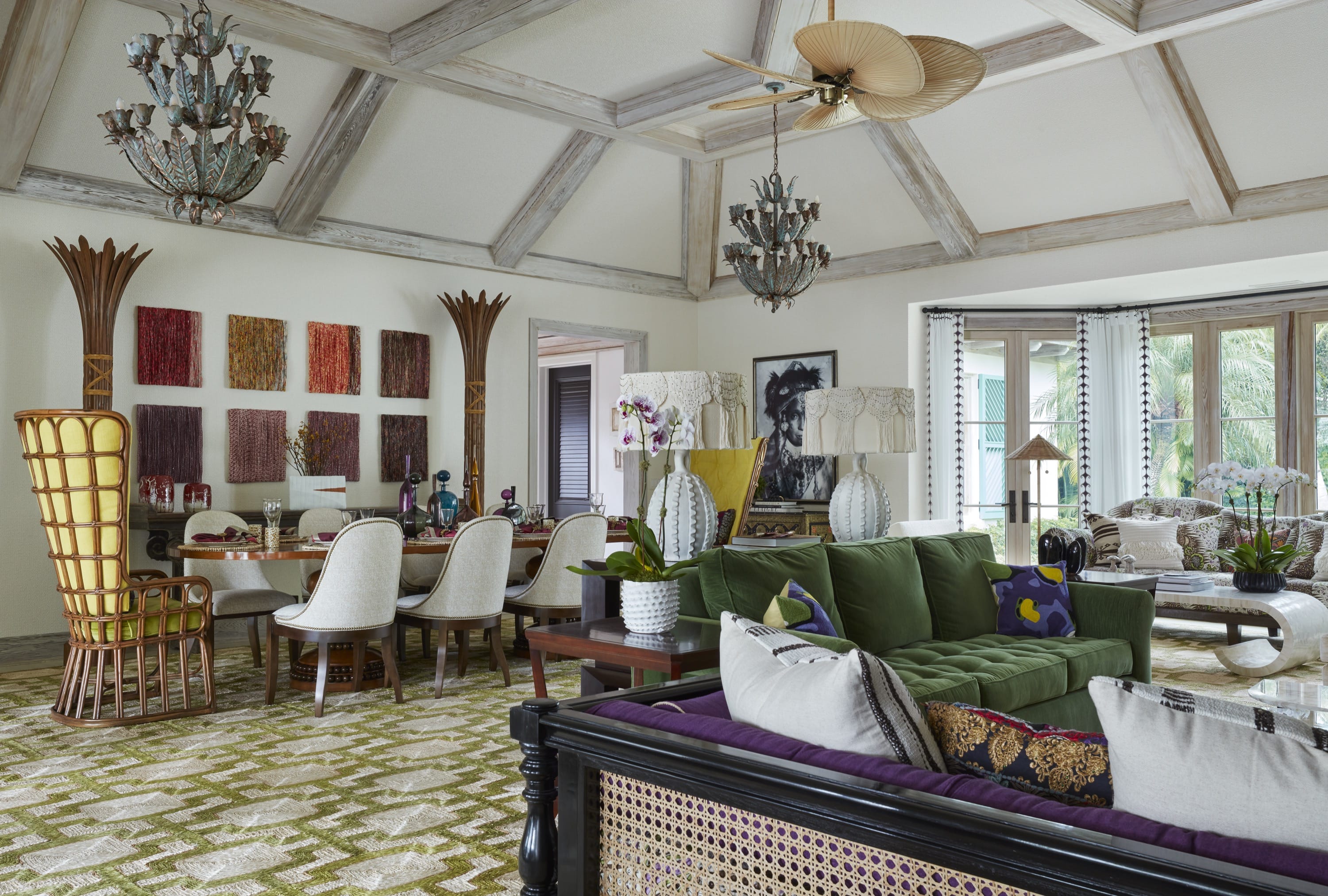 Spacious living and dining room with green sofa, rattan chairs, modern art, and large windows with garden view.