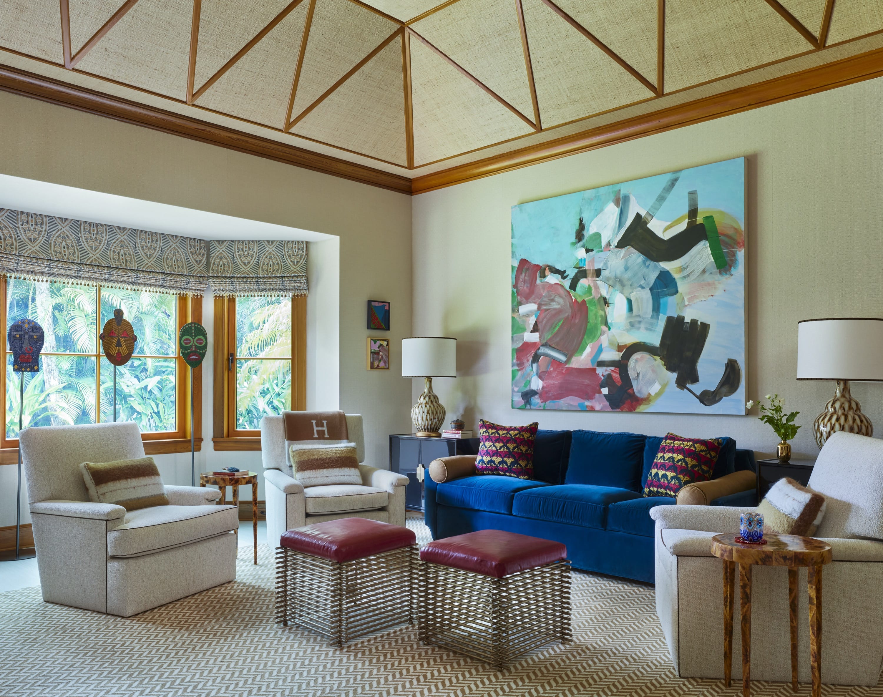 Living room with blue sofa, cream chairs, wooden ceiling, patterned rug, and colorful abstract painting.