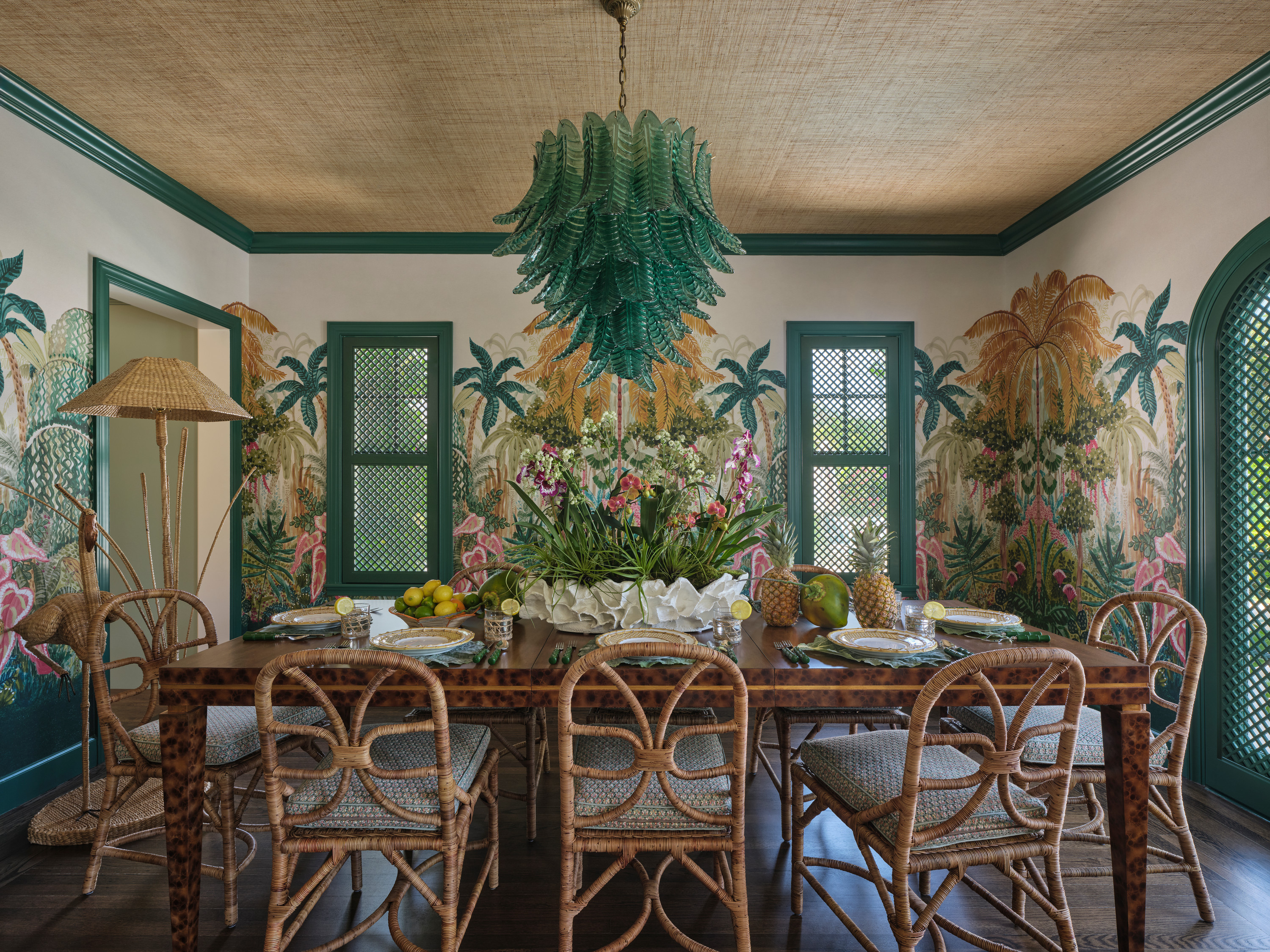 Dining room with tropical wall murals, curved chairs, and a green chandelier.