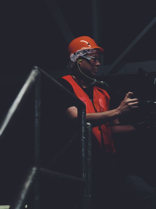 Worker in an orange hard hat and safety vest standing in a dark industrial space
