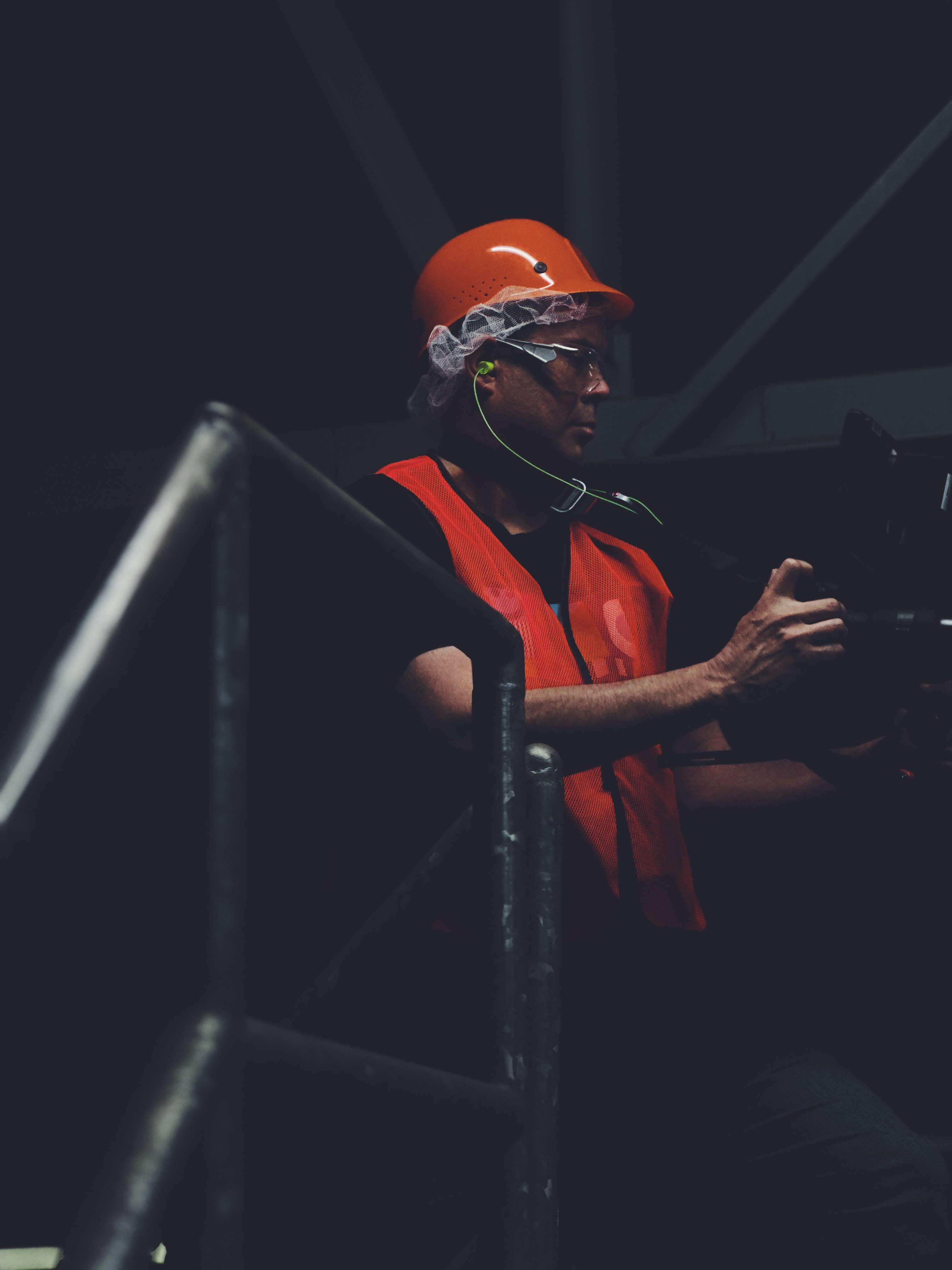 Worker in an orange hard hat and safety vest standing in a dark industrial space