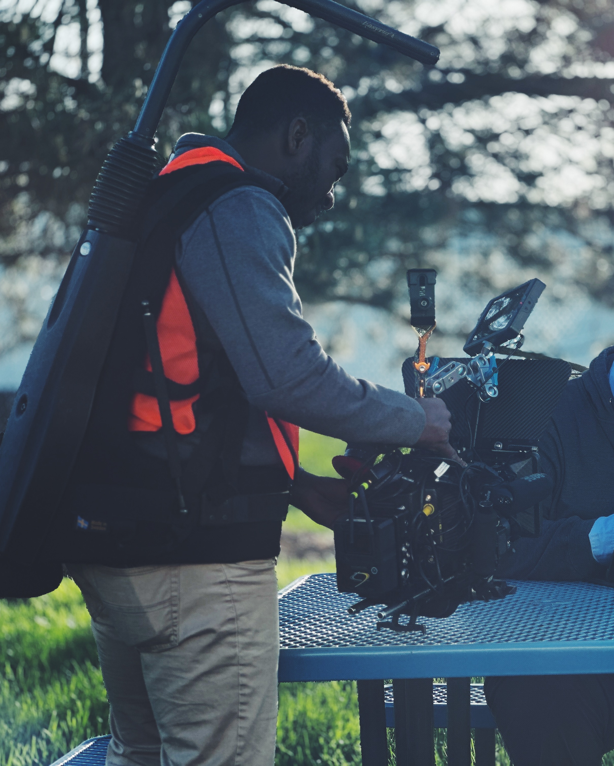 Person in outdoor workwear operating camera equipment beside a table
