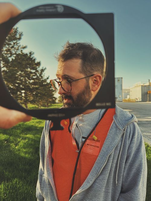 2. Man wearing glasses and an orange safety vest outdoors