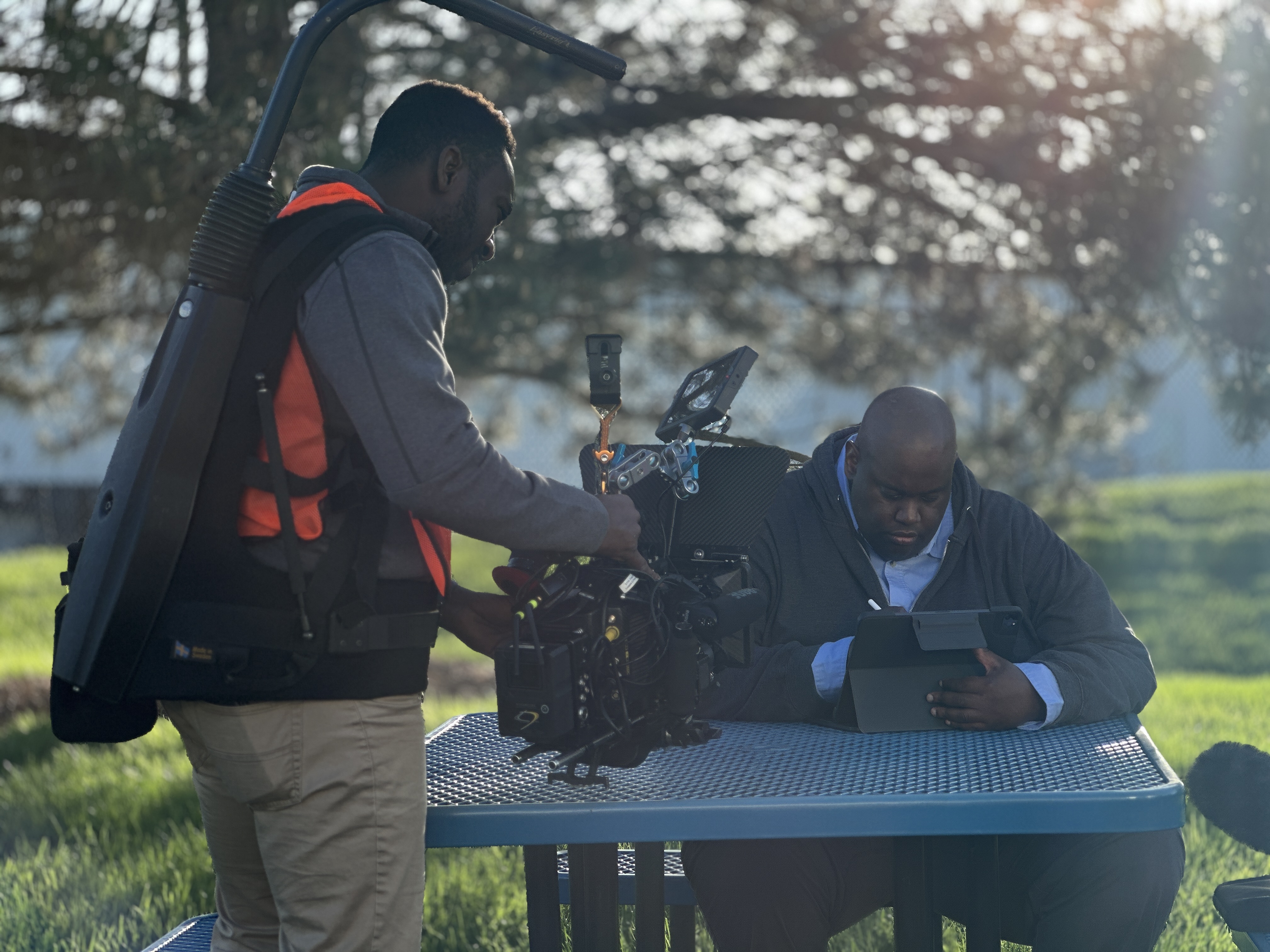 Crew member filming outdoors beside equipment and a work surface