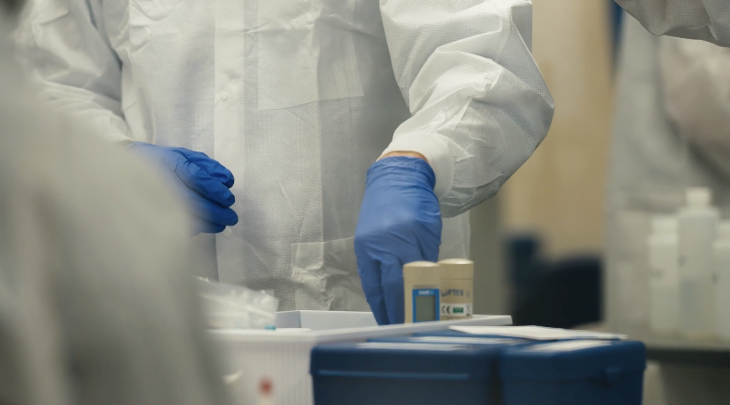 Person in white protective clothing handling equipment on a work surface