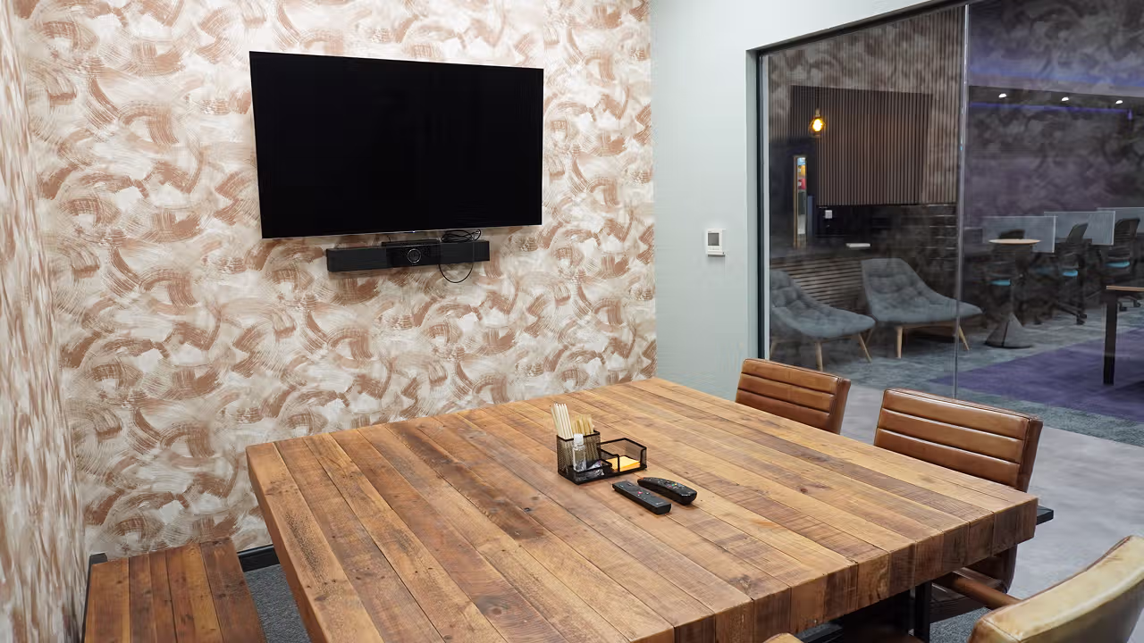View from inside the huddle meeting room. Brown wooden table with leather seating and TV on the wall.