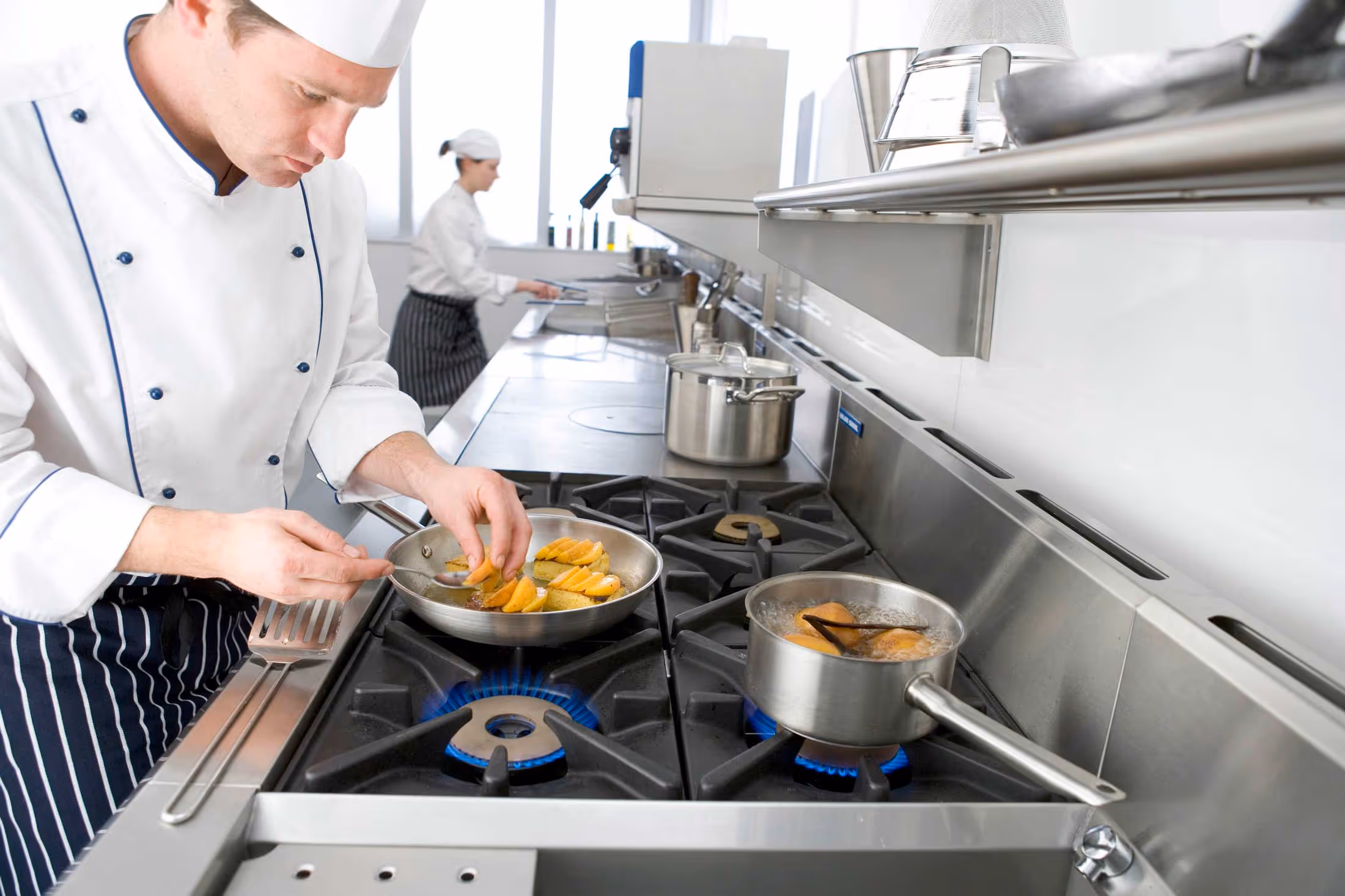 Modern professional kitchen with wooden countertops, stainless steel appliances, and cooking utensils.