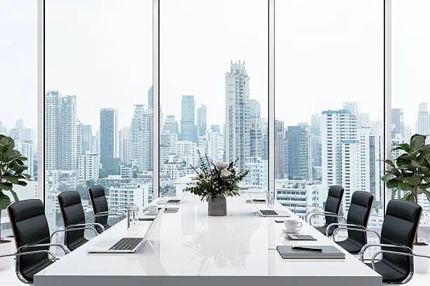 Modern conference room with black chairs, laptops, notebooks, and a floral centerpiece, featuring large windows with a city skyline view.