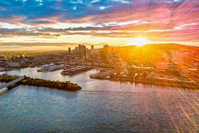 Aerial view of a city skyline at sunset with the sun casting golden rays over buildings and waterfront.