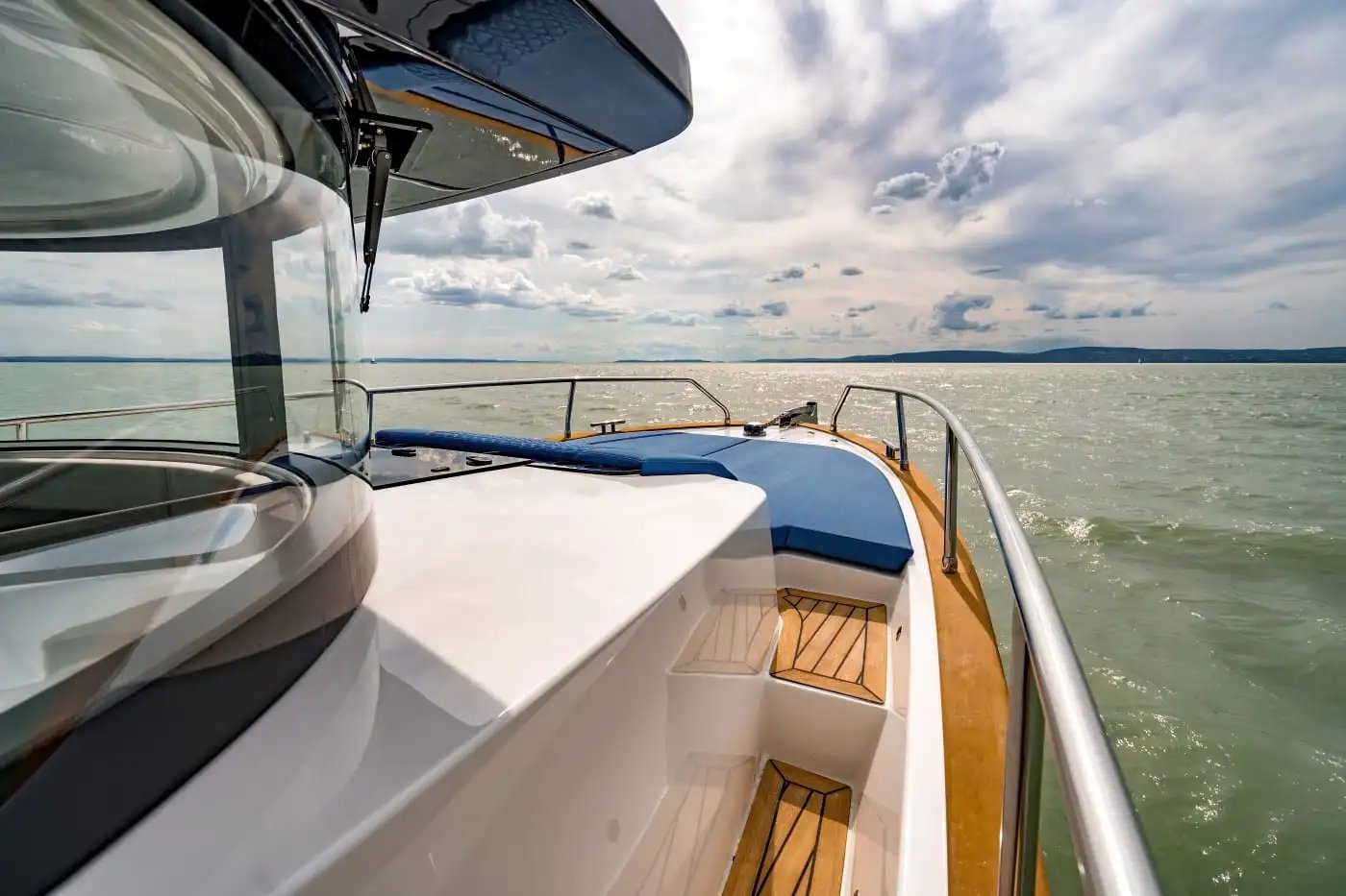 View from the front deck of a boat with blue cushions, overlooking calm water under a partly cloudy sky.