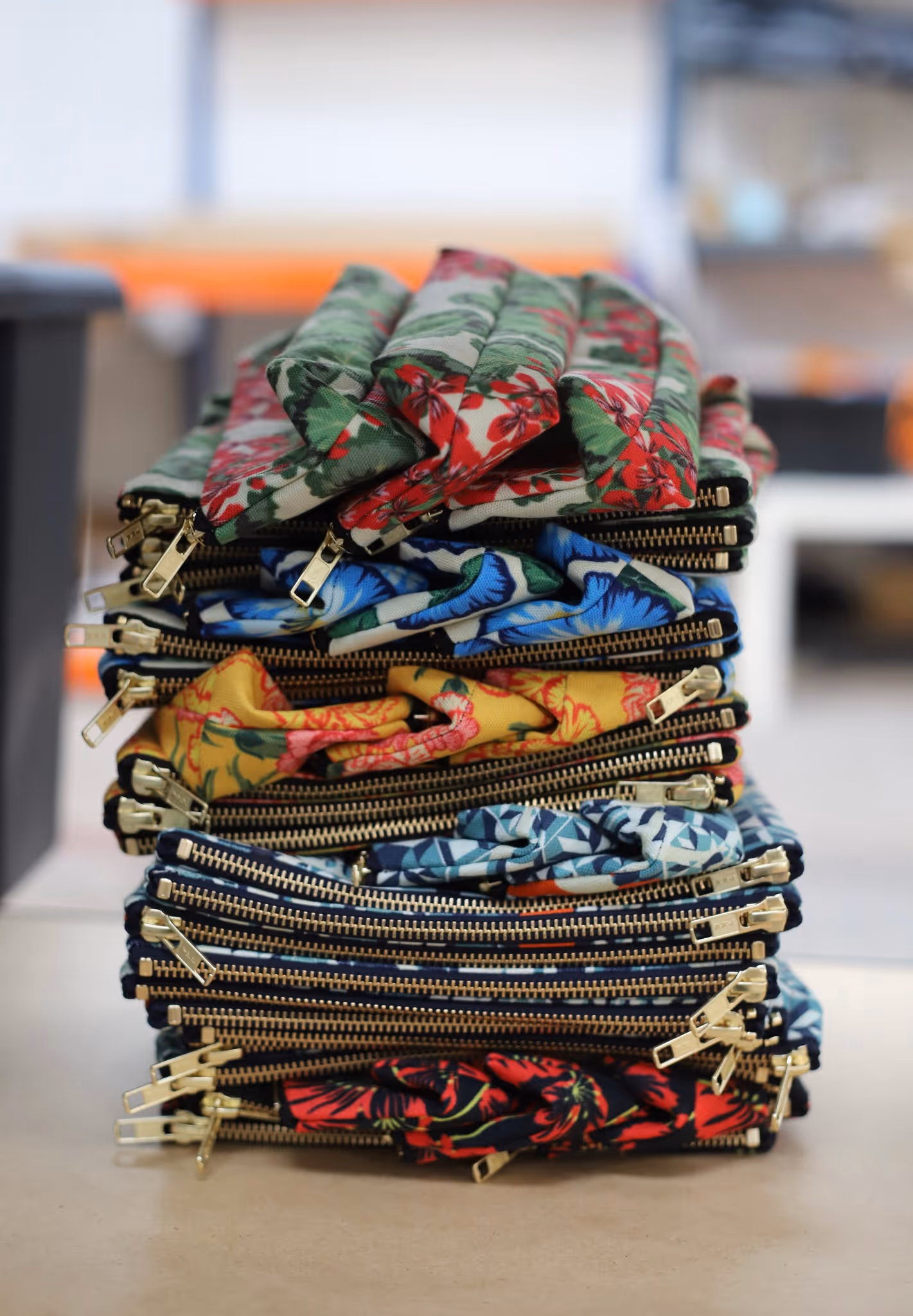 Stack of colorful floral-patterned fabric pouches with gold zippers on a table.
