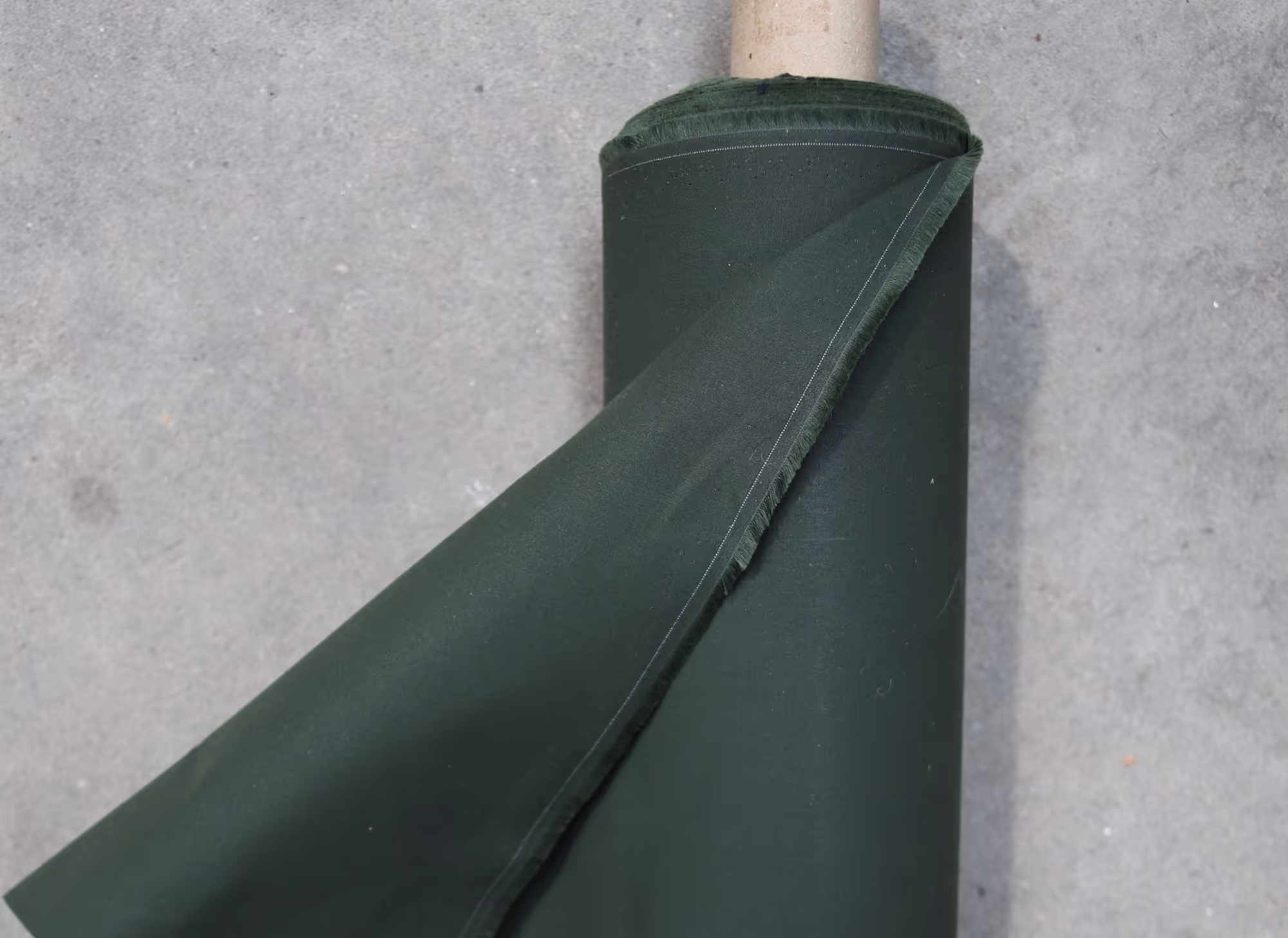 Roll of dark green fabric partially unrolled on a grey surface.