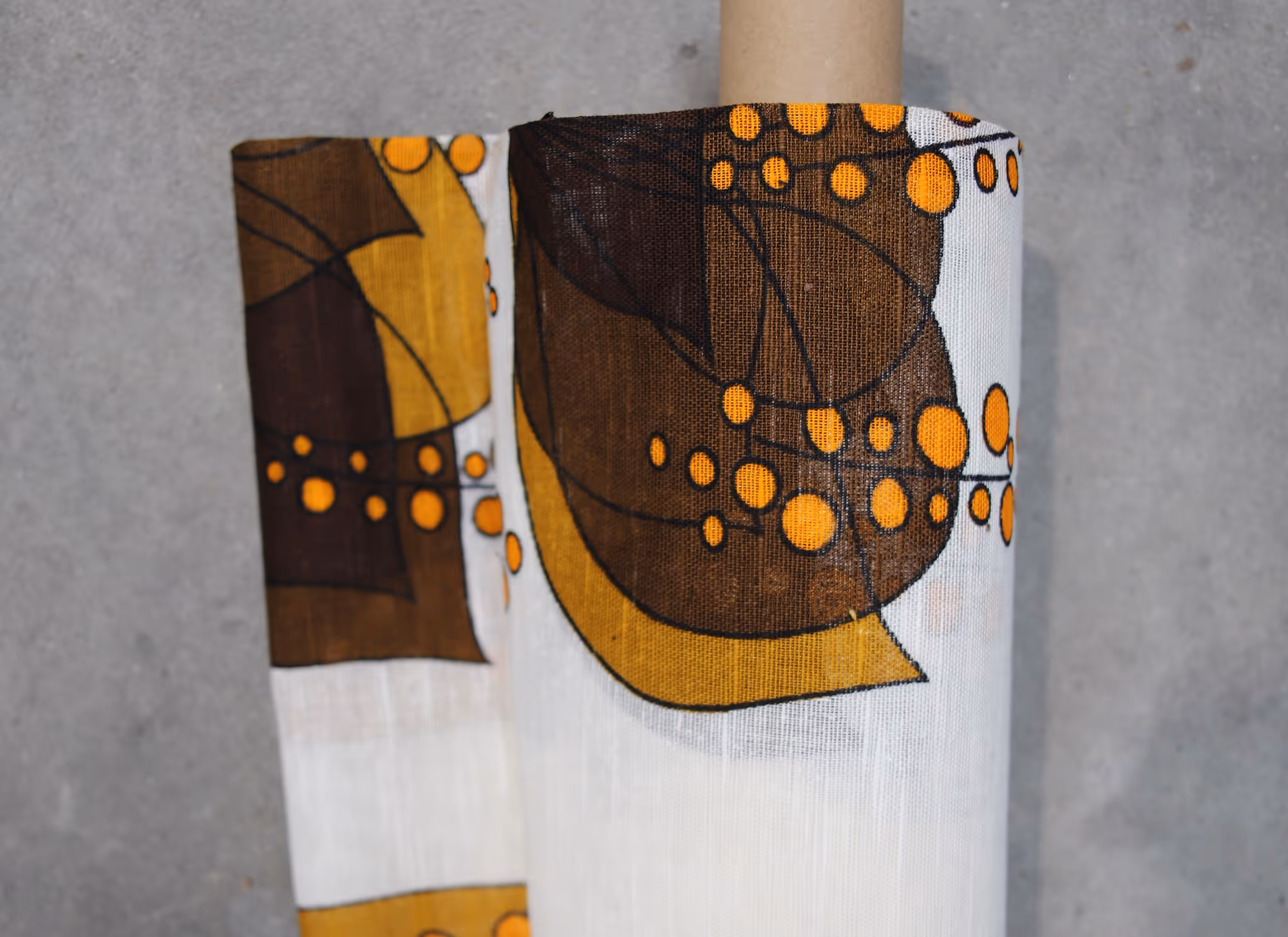 Roll of fabric with a white base featuring abstract brown and yellow shapes and orange dots.
