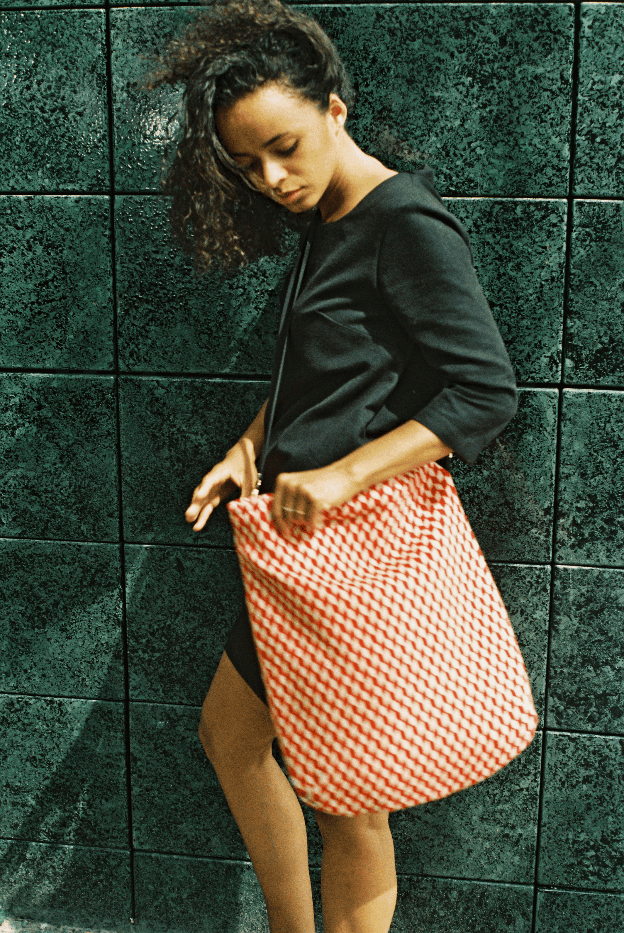 Colorful striped shoulder bag with a black adjustable strap resting against a weathered stone wall.