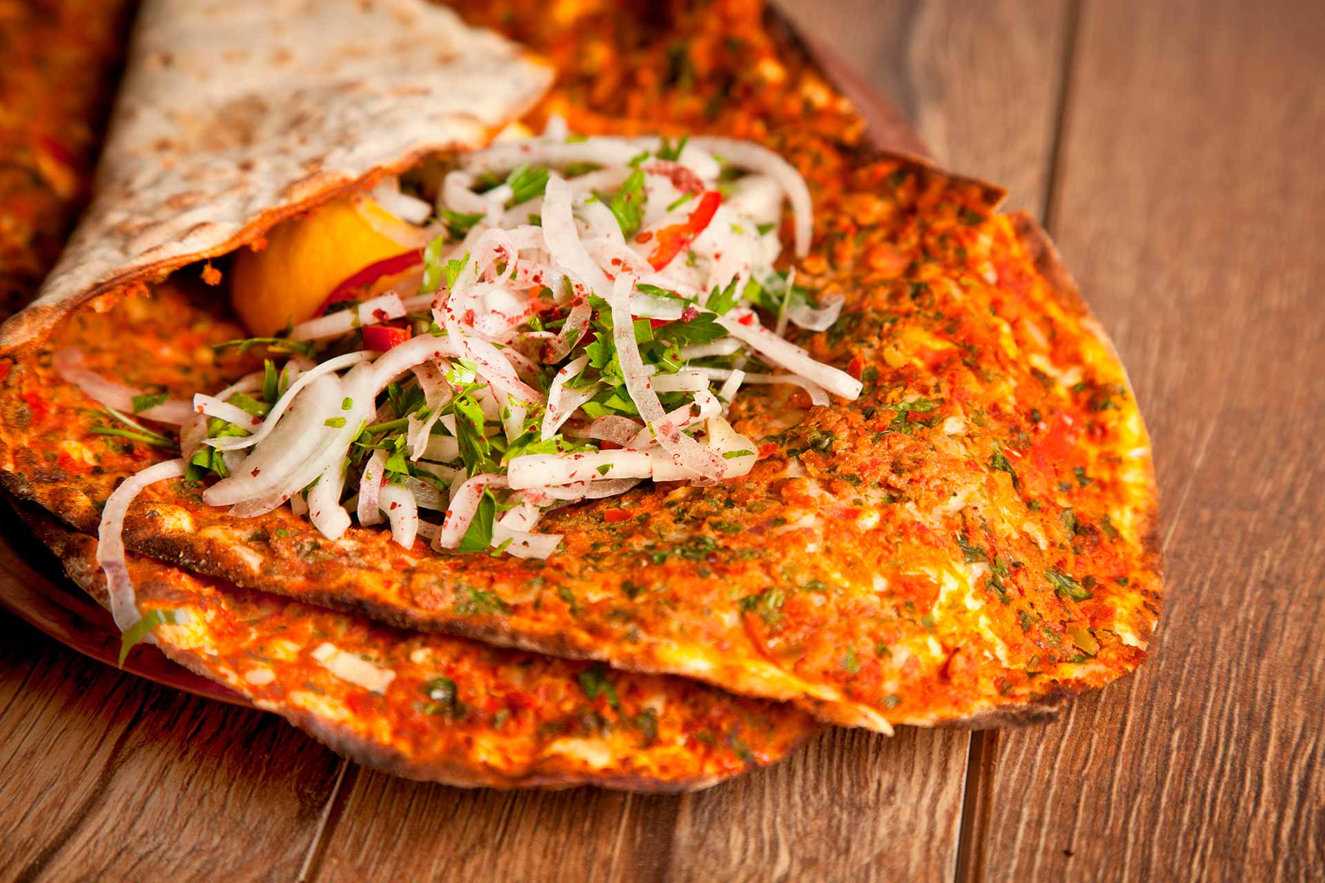 Lahmacun topped with chopped onions and parsley on a wooden surface.