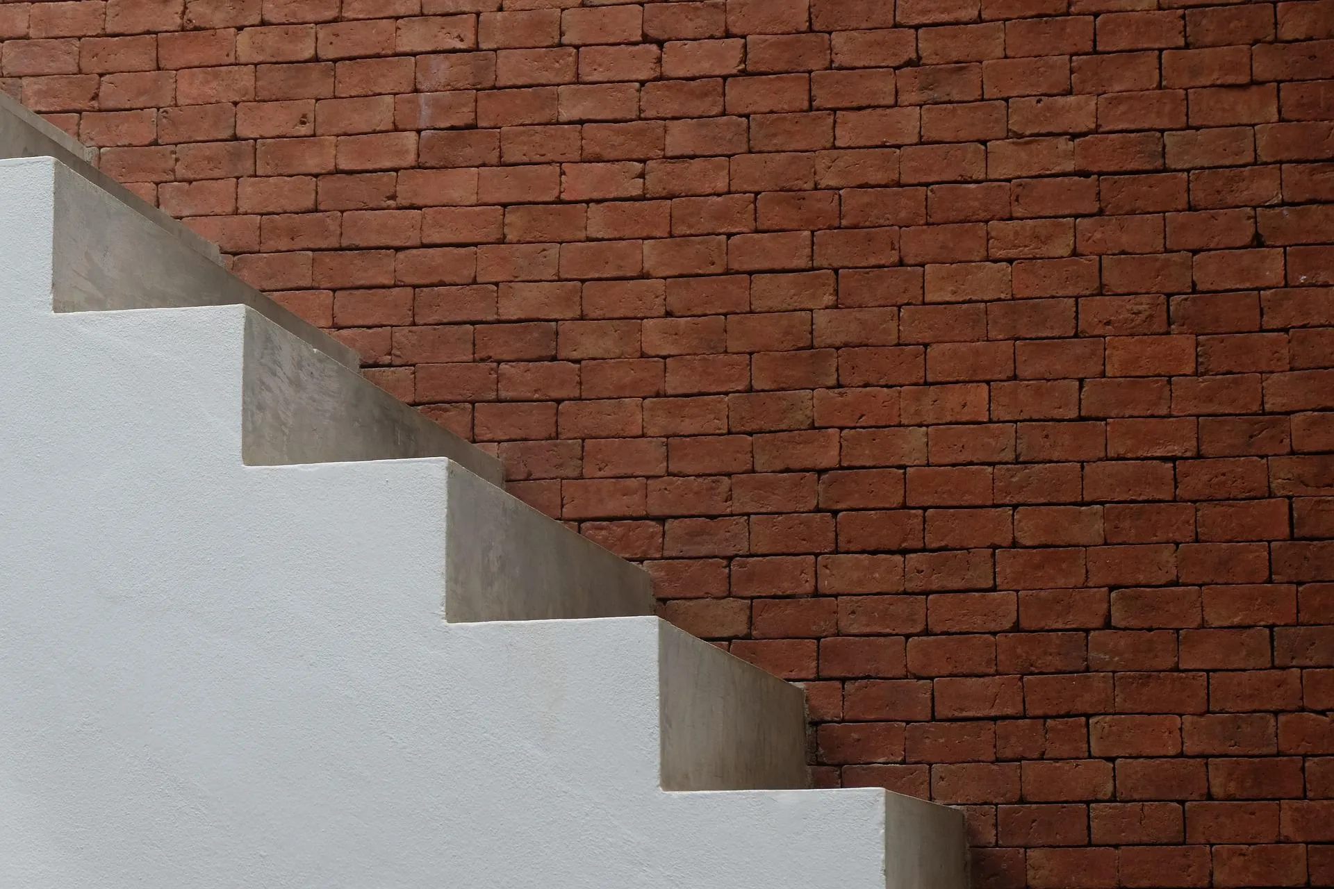 Stairs climbing upwards, against a red brick wall.