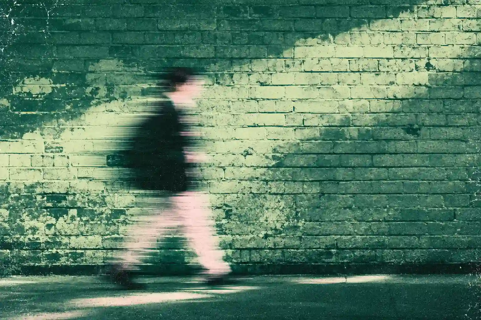 A blurred figure walks past a textured brick wall in muted green tones, symbolising different environments operating within a shared structure.