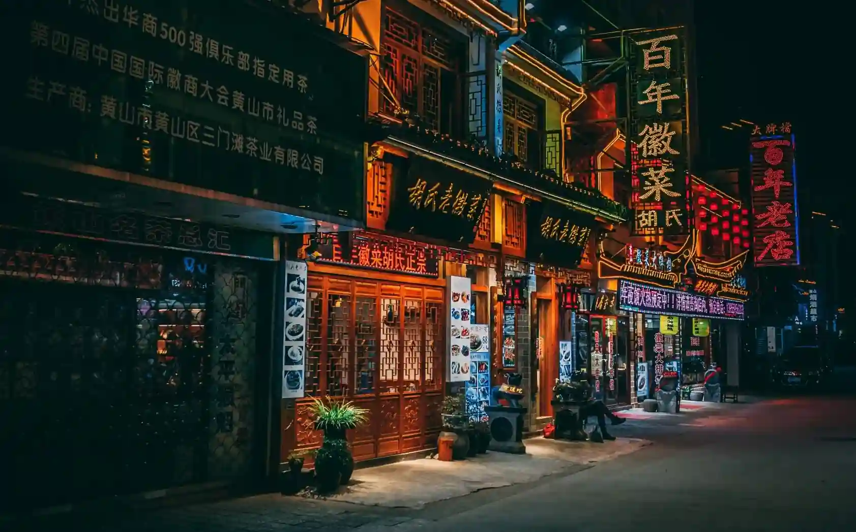 Illuminated traditional Chinese street storefronts at night.