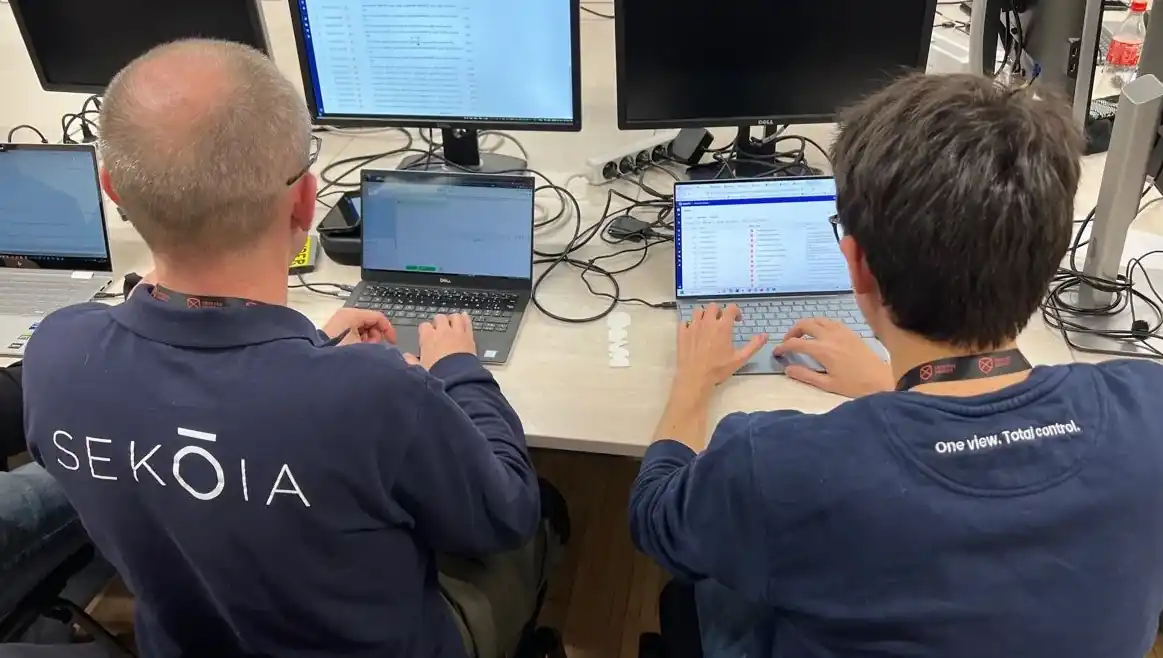 Two Sekoia cybersecurity analysts working on laptops and desktop monitors.
