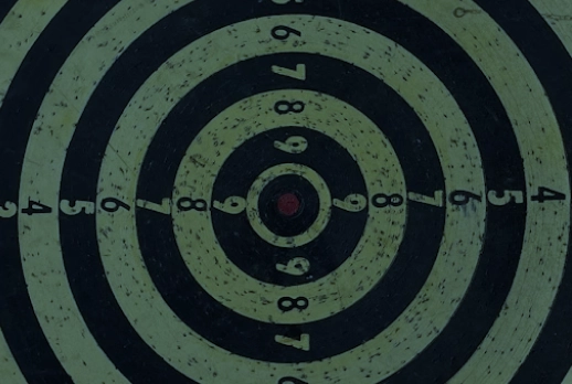 Abstract dark target graphic with concentric circles, radial markings, and a central crosshair.