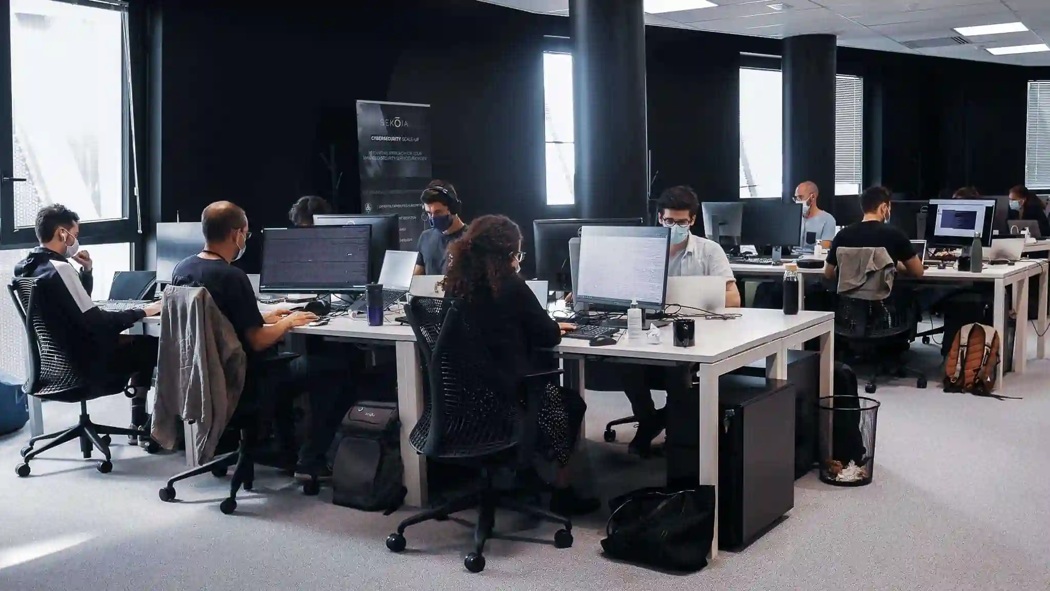 Open-plan office with employees wearing face masks, working at computer desks at Sekoia.