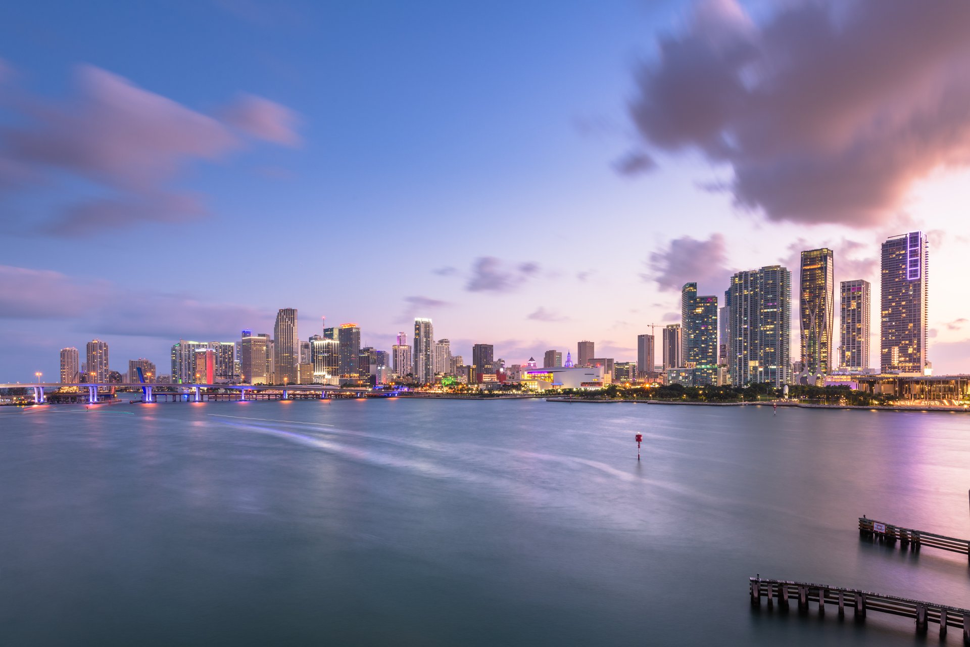 Miami downtown skyline at dusk with illuminated skyscrapers and calm waters in the bay.
