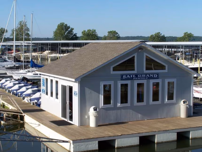 Rental building labeled Sail Grand Rentals on a wooden dock surrounded by sailboats and covered boat slips.