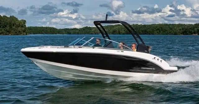 Black and white speedboat with three people cruising on a lake with tree-covered shore in the background.