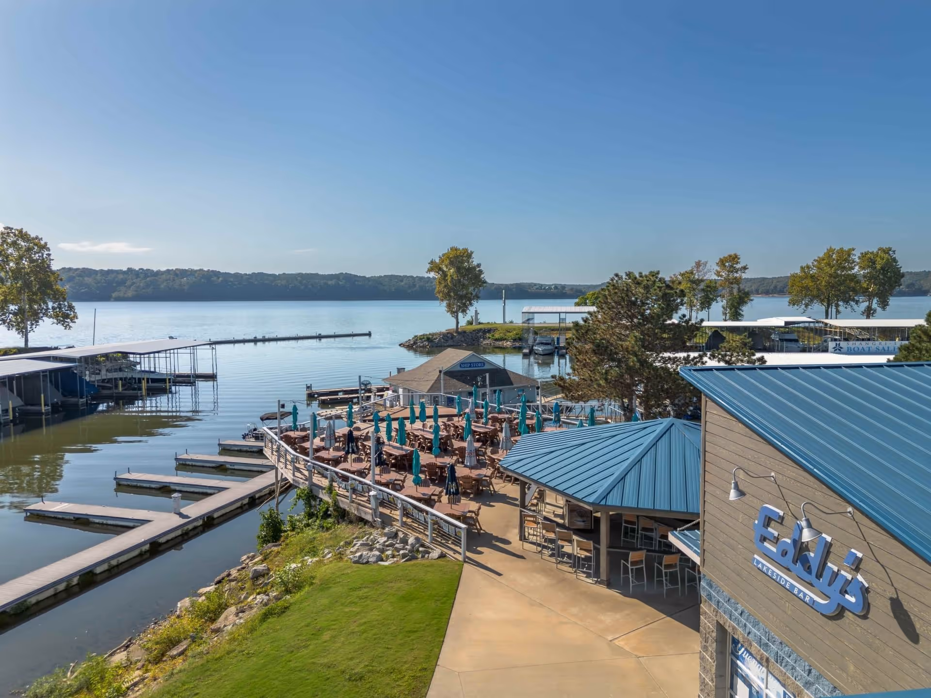 Outdoor seating area with umbrellas and docks by a lakeside bar named Eddy's on a clear day.