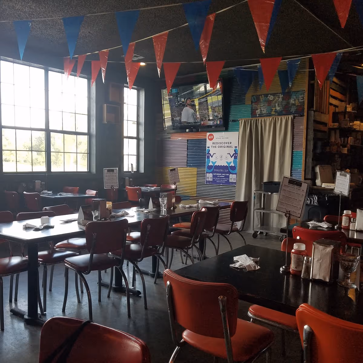 Empty diner with red chairs, tables set with napkins, and red and blue pennants hanging from ceiling.