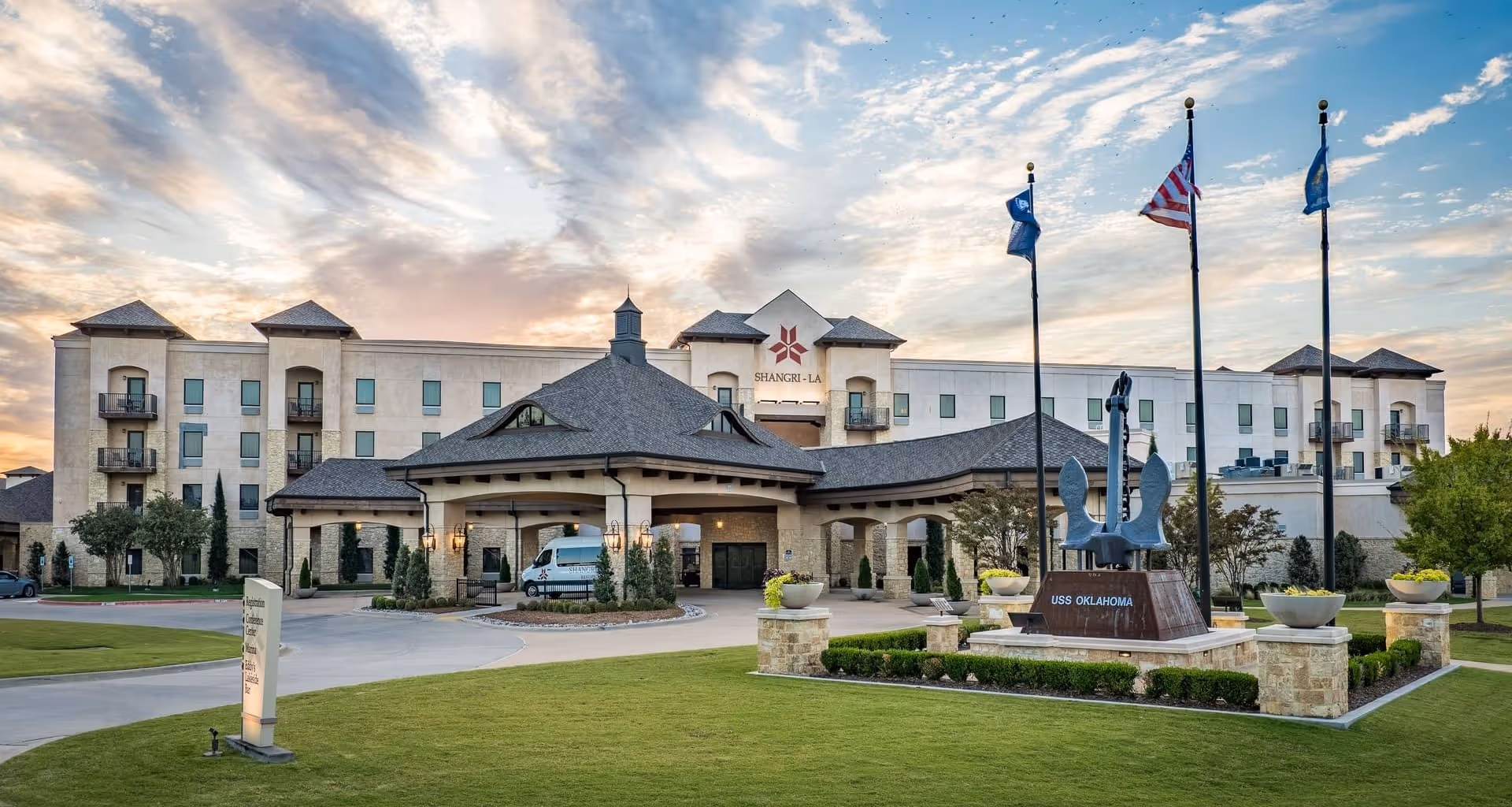 Exterior of Shangri-La hotel with green lawn and USS Oklahoma anchor monument at sunset.