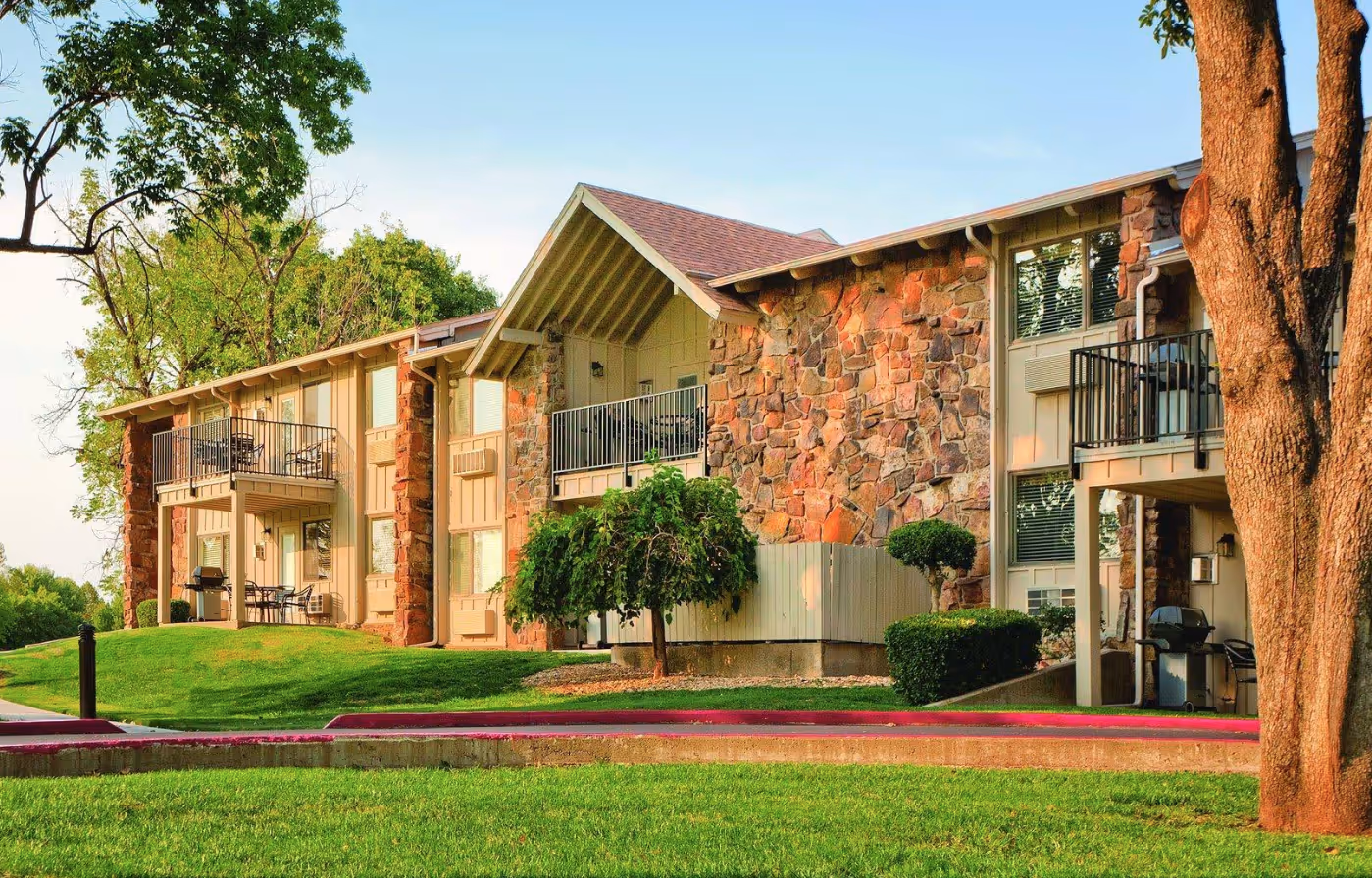 Exterior of a two-story apartment building with stone and wood facade, balconies, and green lawn.