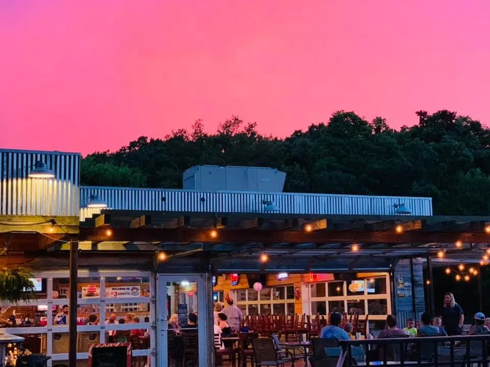 Outdoor restaurant seating at dusk with people dining under string lights and a pink sky.