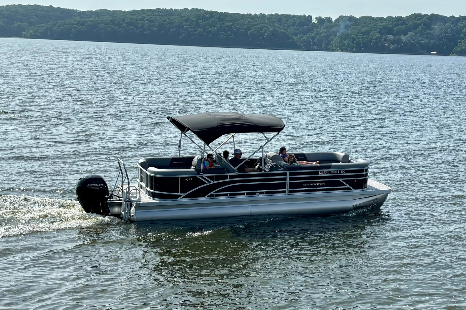 Black Bennington pontoon boat with canopy cruising on a lake carrying five people.