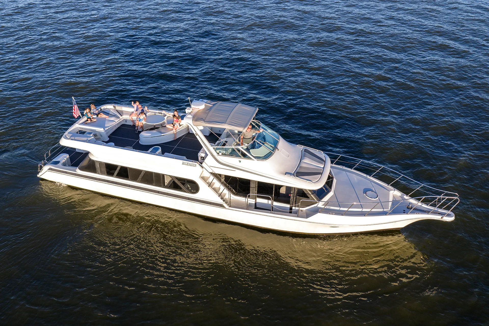 White luxury boat named Bluewater with people on upper deck cruising on water.
