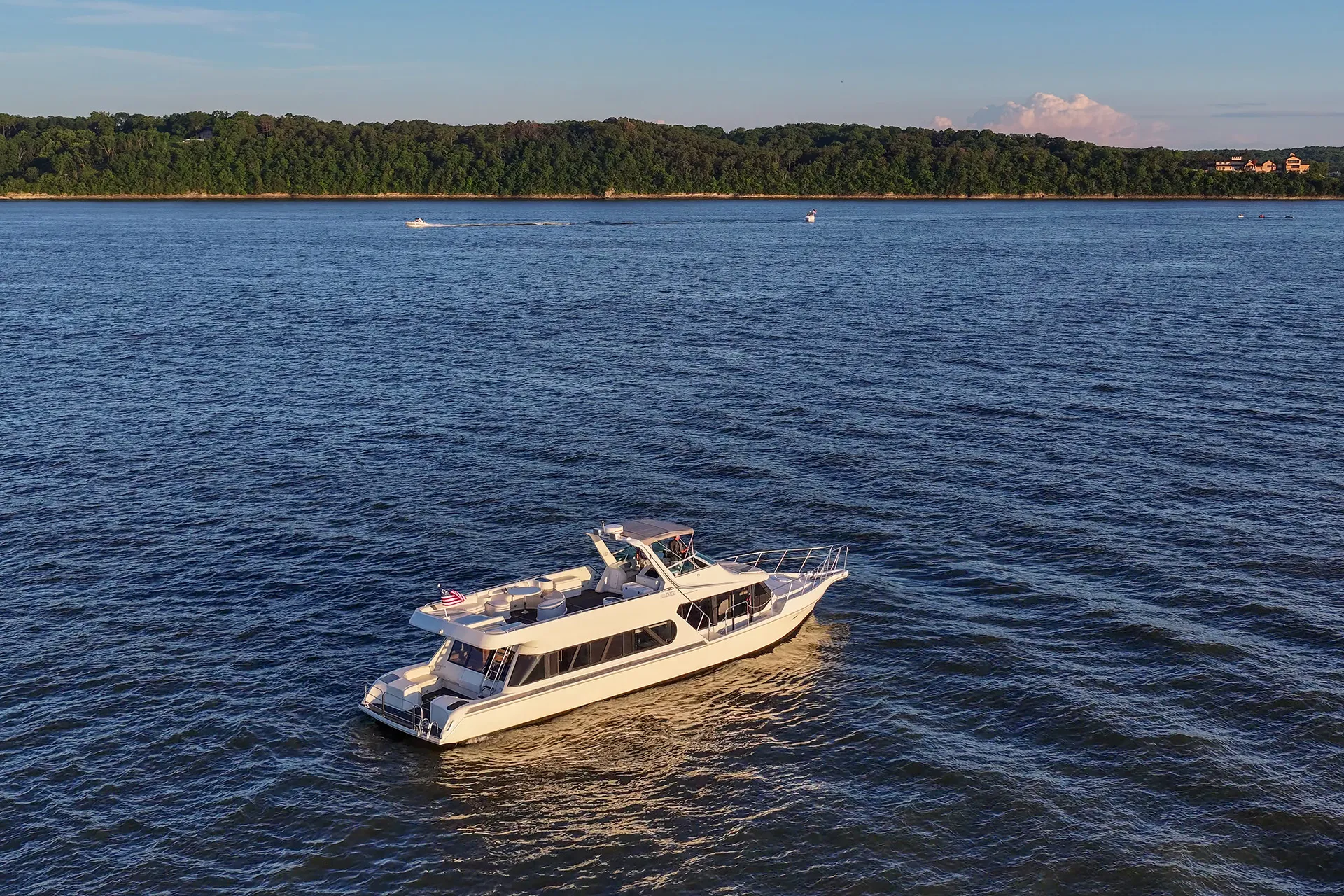 White yacht cruising on blue waters near a tree-lined shore under a clear sky.