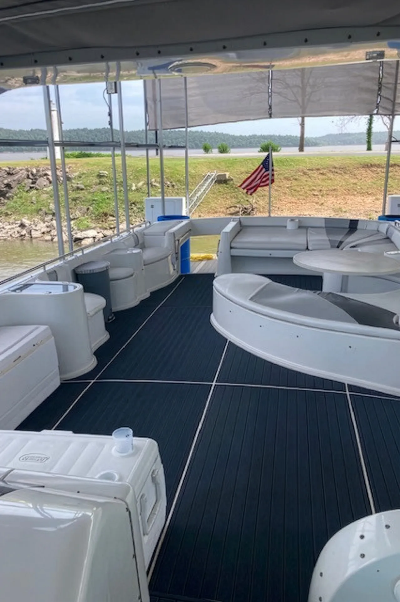 Spacious boat deck with white cushioned seating, a round table, and an American flag in the background.