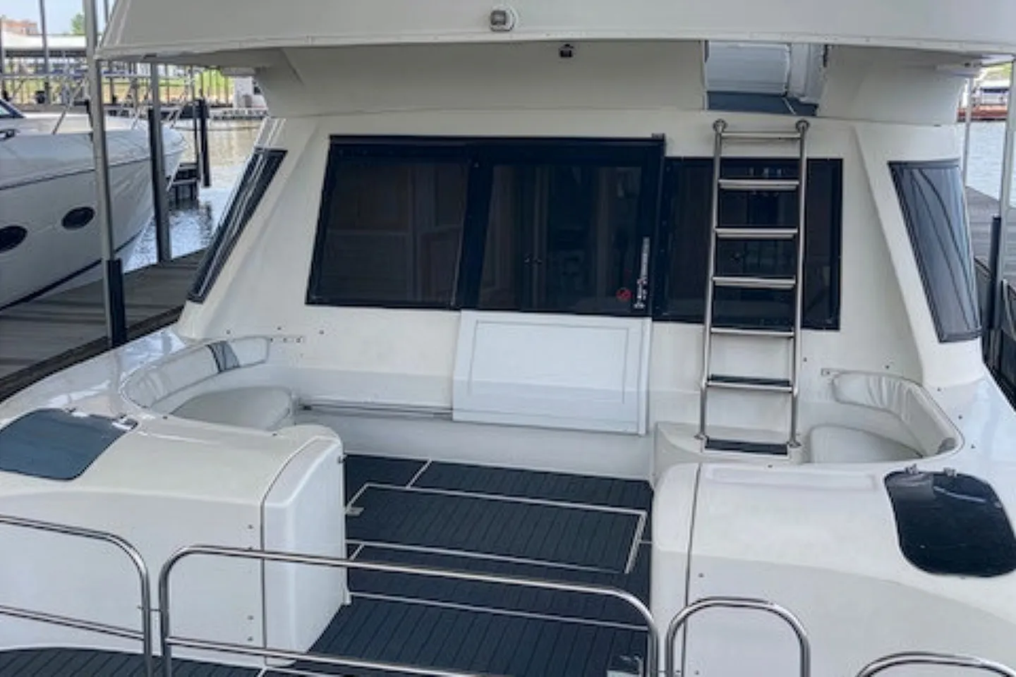 Rear deck of a white yacht with seating, a metal ladder, and sliding tinted windows.